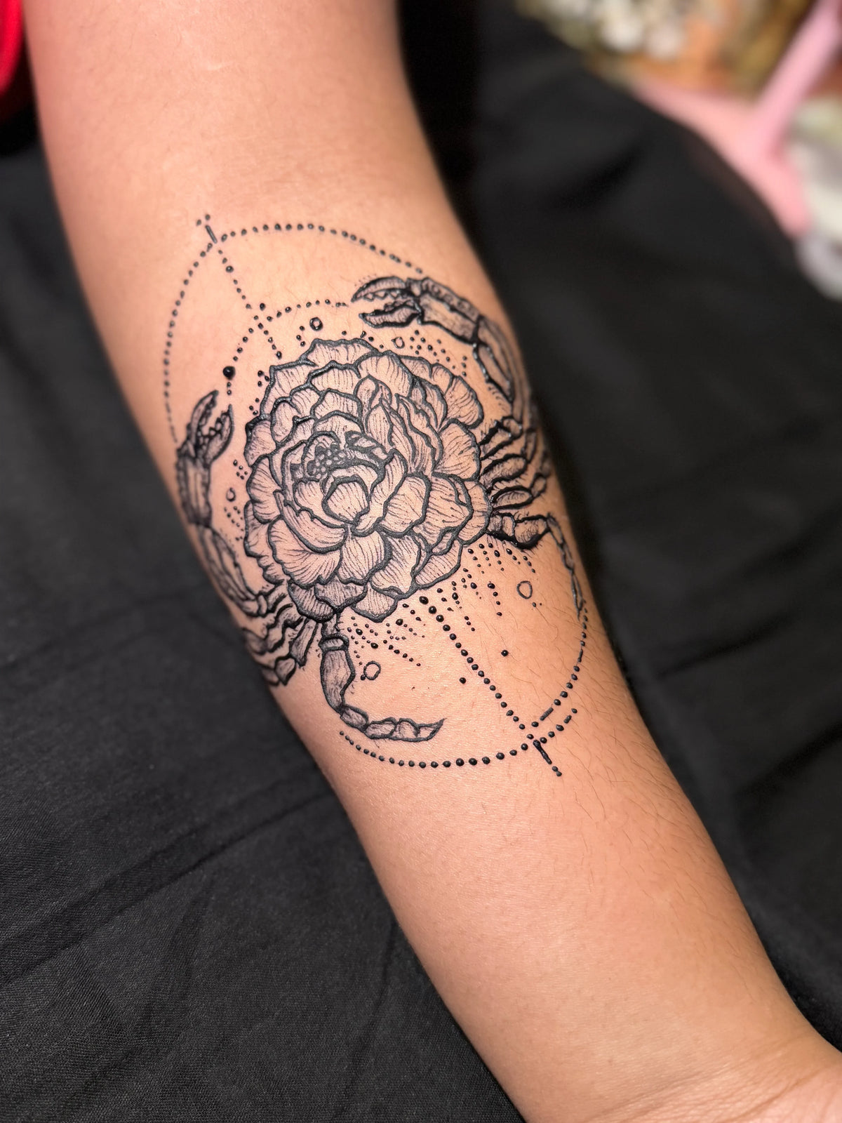 Henna design of a flower and scorpion fusion on forearm with dotted geometric accents