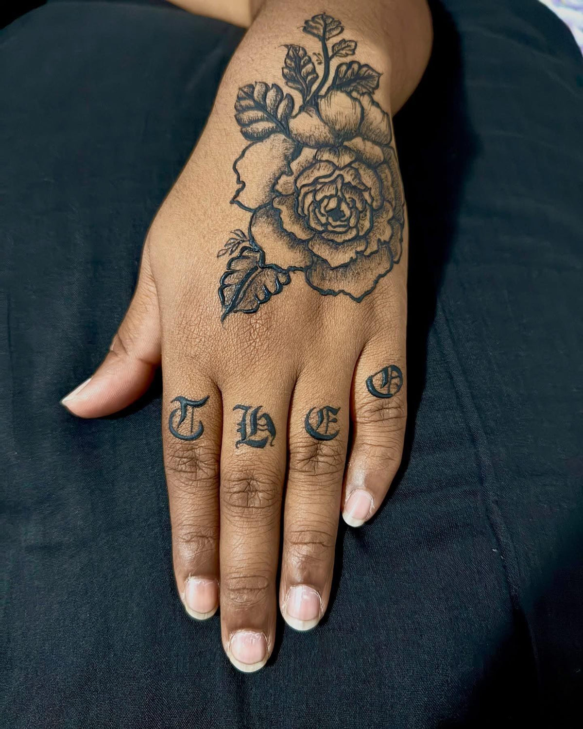 Hand with detailed black rose henna art and bold letter designs on fingers