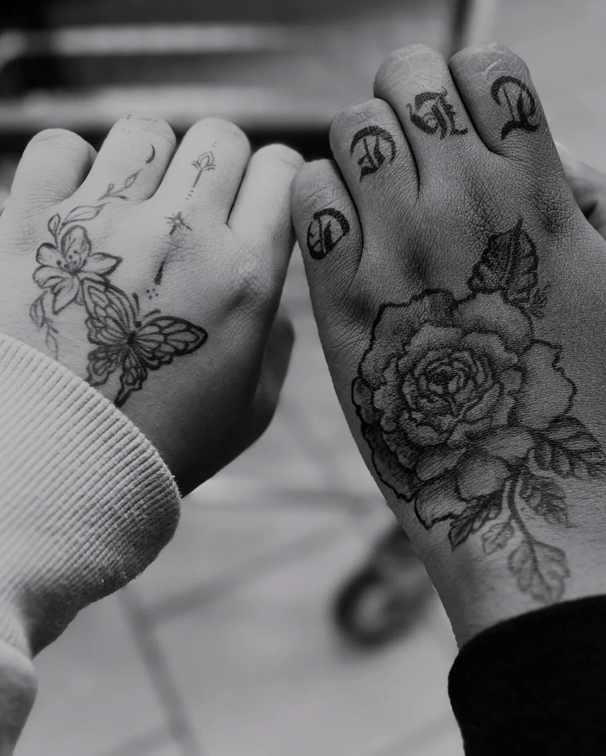 Black and white photo of two hands with detailed henna flower and butterfly designs.
