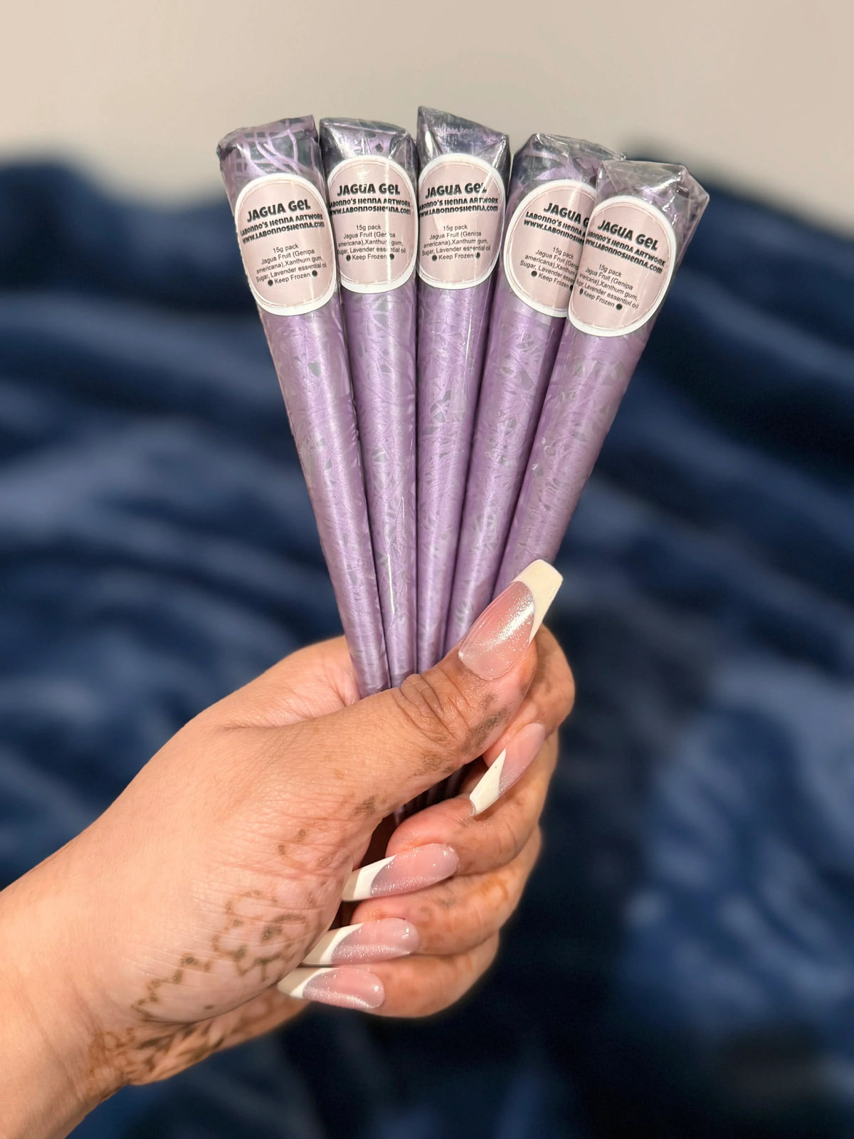 Hand with henna design holding five purple jagua gel cones for body art