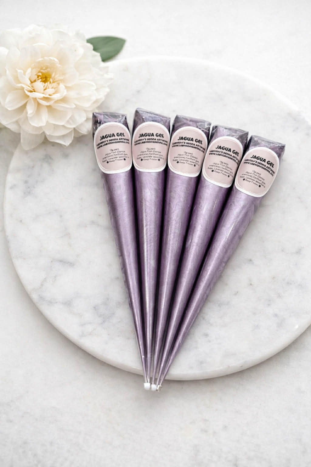 Five metallic purple jagua gel cones for body art on a marble plate with a white flower.