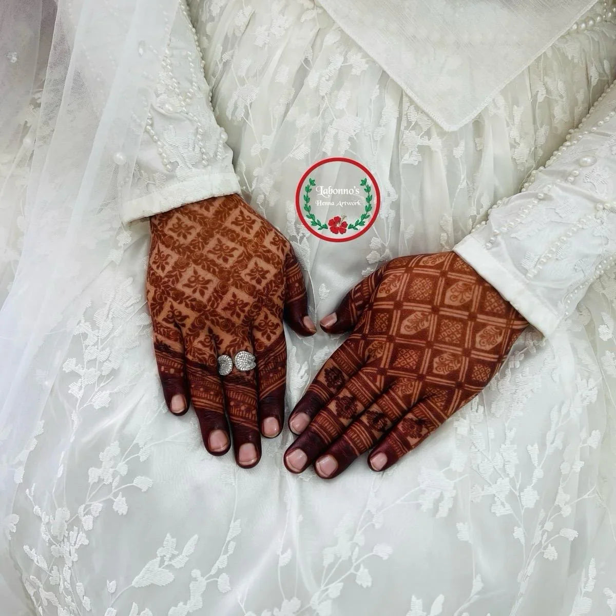 Bridal hands with intricate henna designs and rings on white lace dress