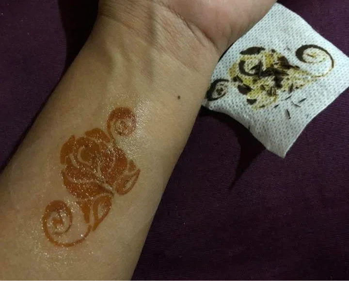 Henna rose floral design on forearm with tissue removing dried henna, body art