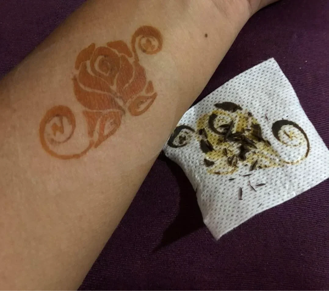 Henna rose design on forearm with peeled stencil on tissue, body art closeup