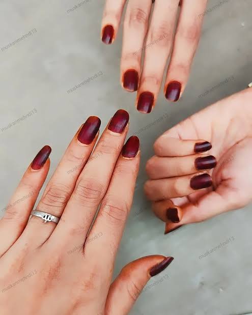 Hands with deep maroon henna-stained nails, showcasing simple henna artwork.