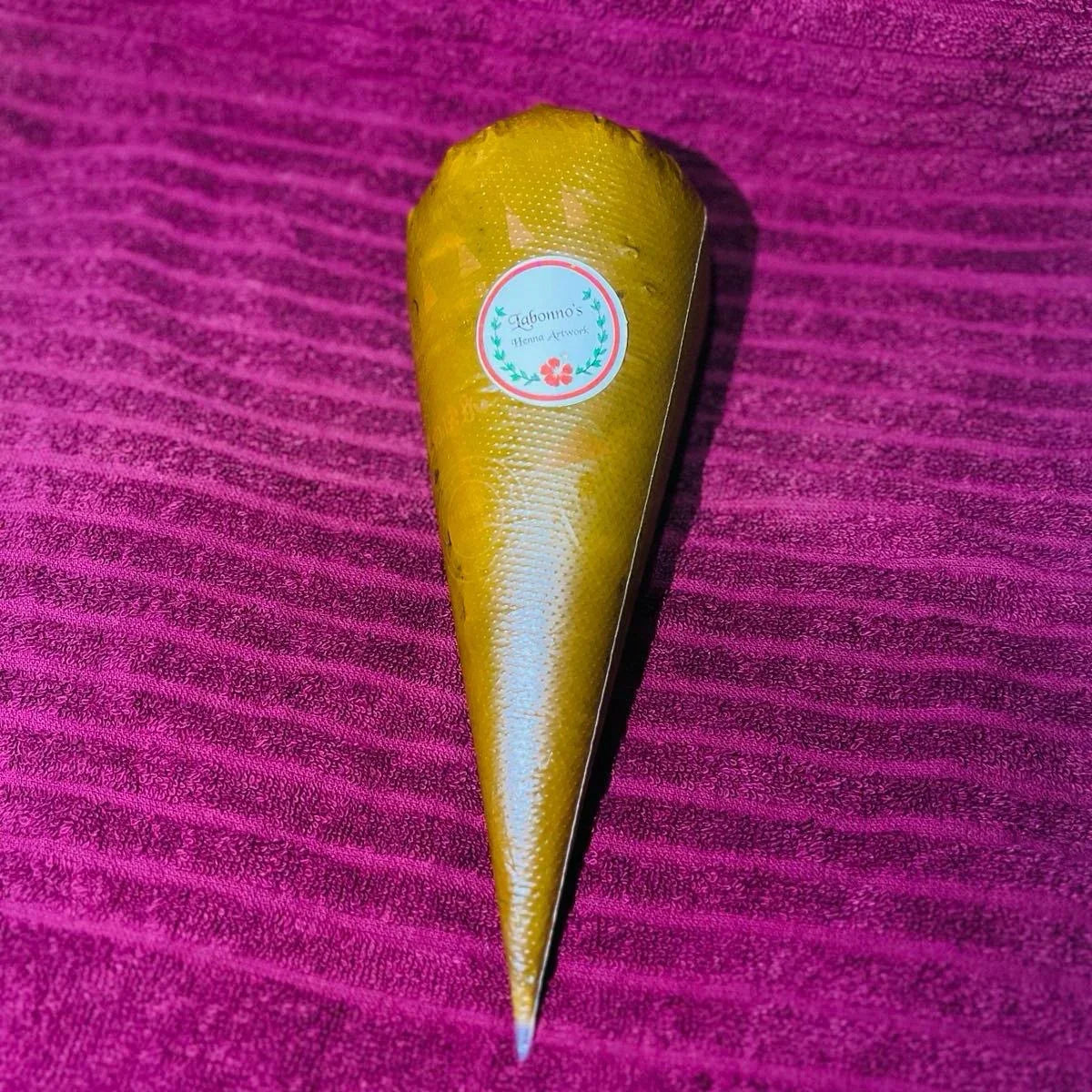 Henna cone with a label on a textured purple background, natural dye body art product.