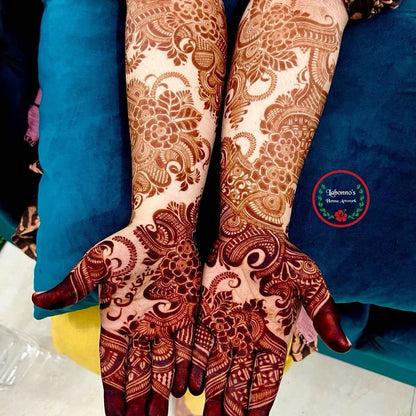 Intricate floral and paisley henna designs on both hands against a blue cushion background