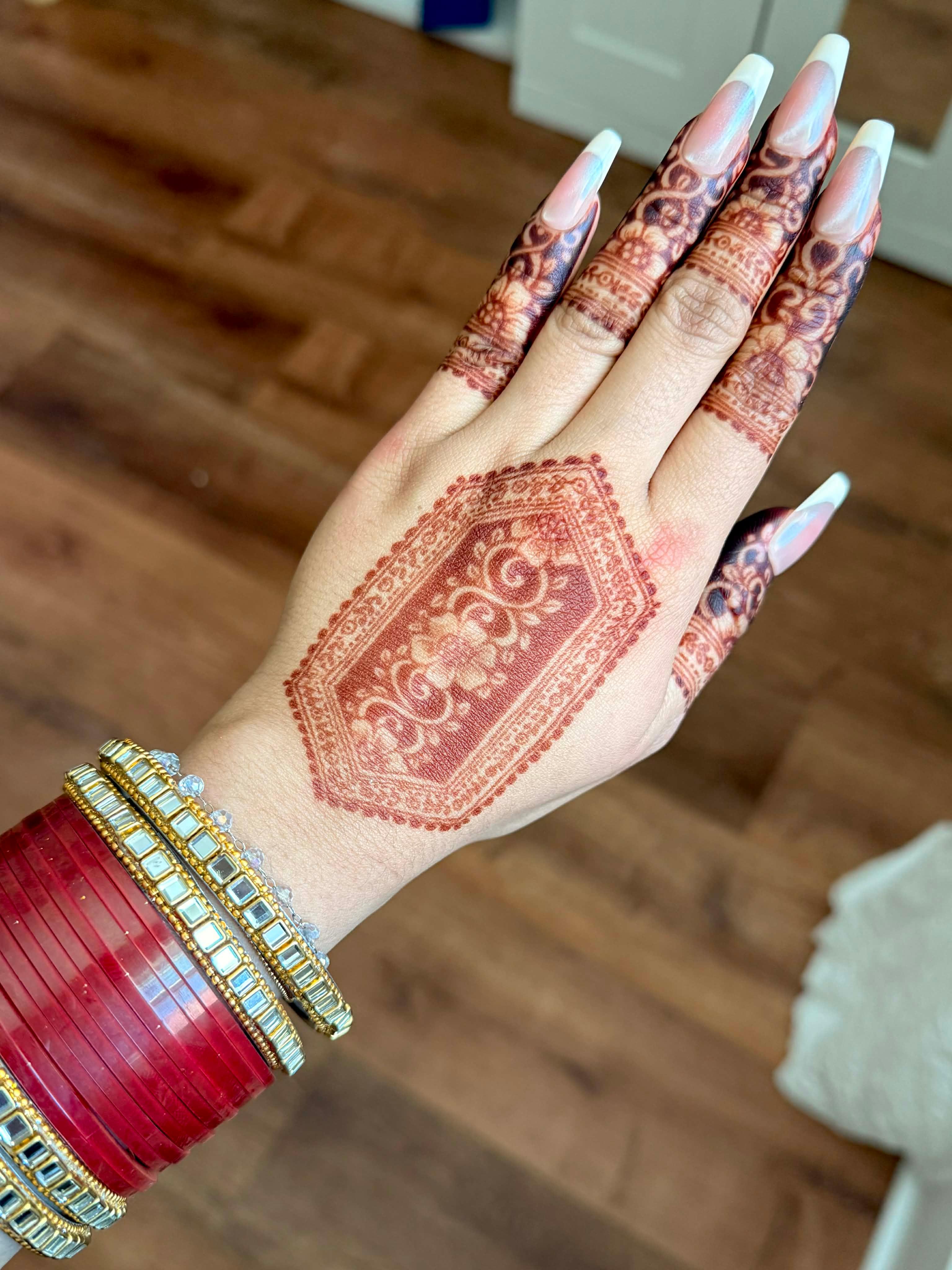 Hand with intricate henna design, red bangles, and long manicured nails on wooden floor