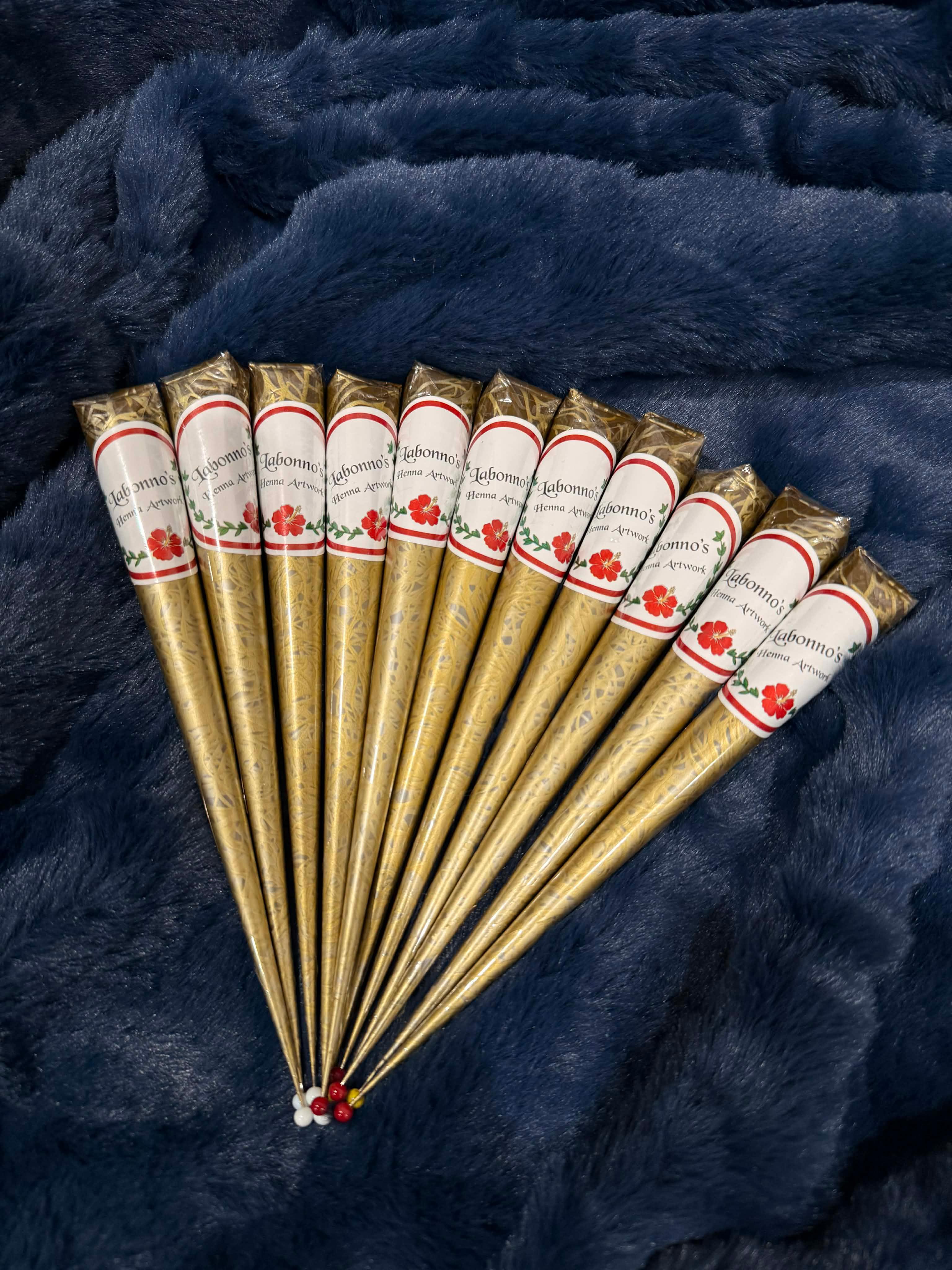 Henna cones arranged on blue fabric, gold wrappers with floral labels, ready for body art