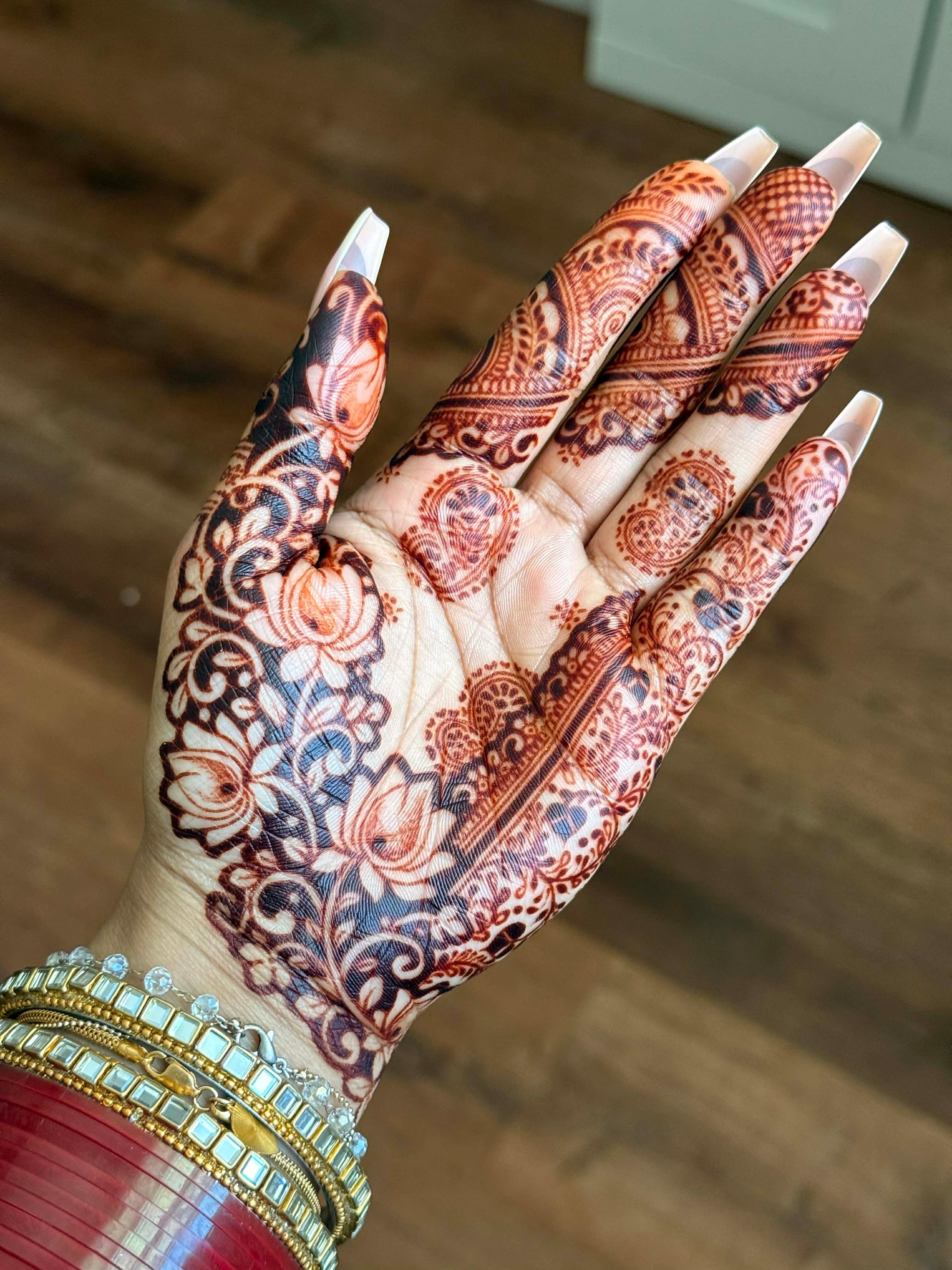 Intricate henna design on palm with floral patterns, bracelets, and long nails